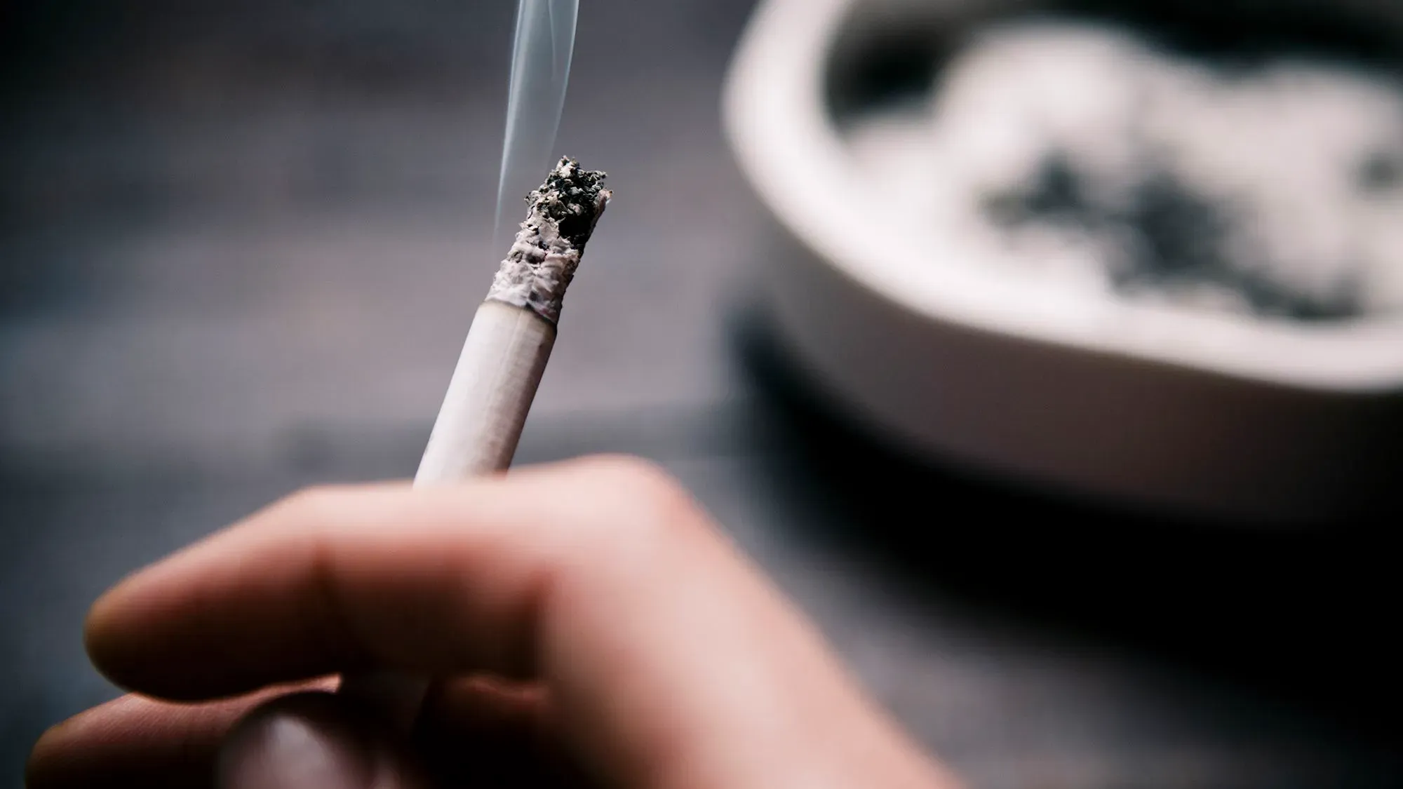 سيجارة مشتعلة في يد شخص، مع وجود رمادها في طبق قريب، تشير إلى مخاطر التدخين المرتبطة بسرطان عنق الرحم.