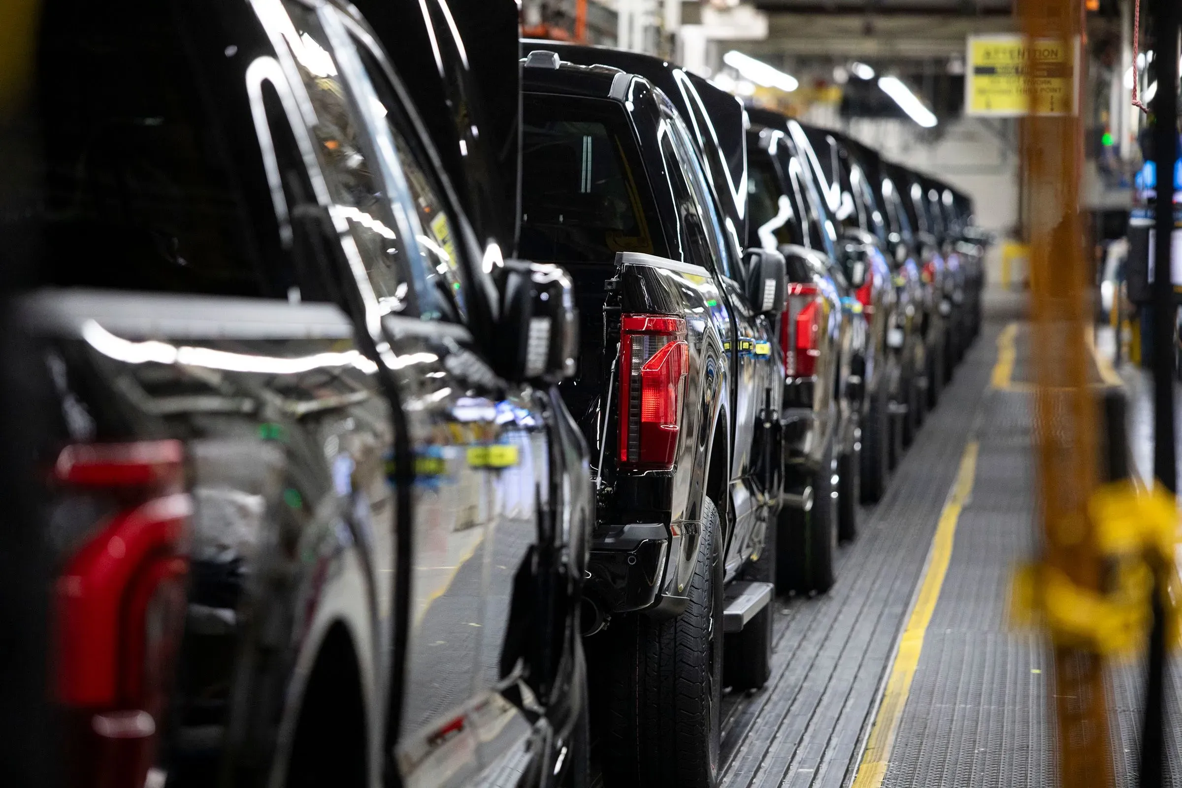 صف من الشاحنات السوداء الجديدة في مصنع تجميع السيارات، تعكس تأثير التعريفات الجمركية على صناعة السيارات الأمريكية.