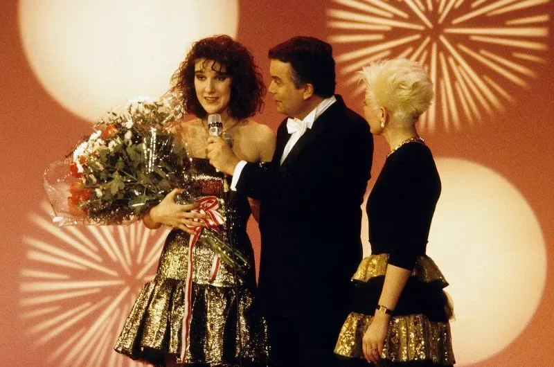 سيلين ديون تتسلم جائزة يوروفيجن عام 1988، مرتدية فستانًا لامعًا، وتظهر مع مقدمي البرنامج، في لحظة تاريخية لمسابقة الأغنية.