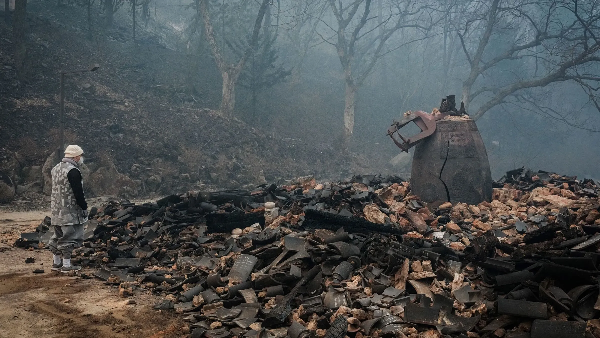 رجل يقف أمام بقايا معبد بوذي محترق في منطقة أويسيونغ، بعد حرائق غابات مميتة في كوريا الجنوبية، مع بقايا دمار حوله.