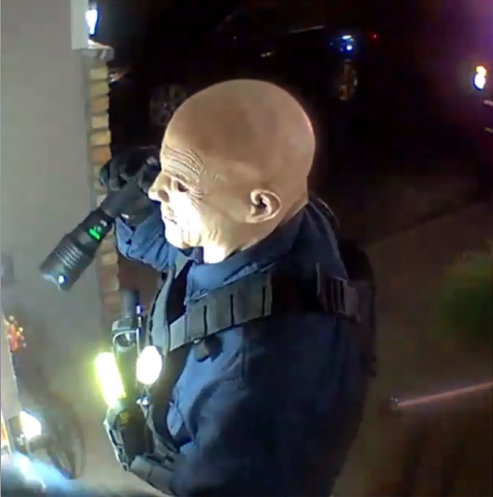 شخص يرتدي زي ضابط شرطة ويحمل مصباحًا، يظهر في مشهد مشبوه، مما يعكس تصاعد العنف السياسي في الولايات المتحدة.