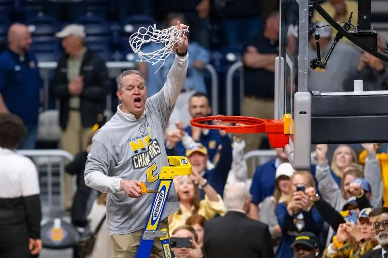 مدرب تشاتانوغا يحتفل بفوز فريقه ببطولة NIT بعد مباراة مثيرة، بينما يقطع الشبكة في أجواء احتفالية مع الجماهير.