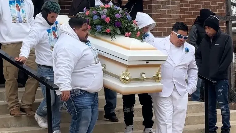 مشهد مؤثر لجنازة جوسلين روخو كارانزا، حيث يحمل المعزون النعش المزهر خارج المدرسة، مع تعبيرات حزن واضحة على وجوههم.