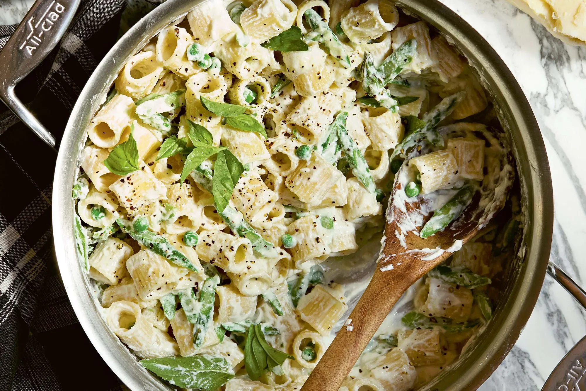 مكرونة كريمية مع الريكوتا والبازلاء في وعاء، مزينة بأوراق الريحان والفلفل الأسود، تعكس وصفة سهلة ولذيذة من كتاب سامين نصرت.