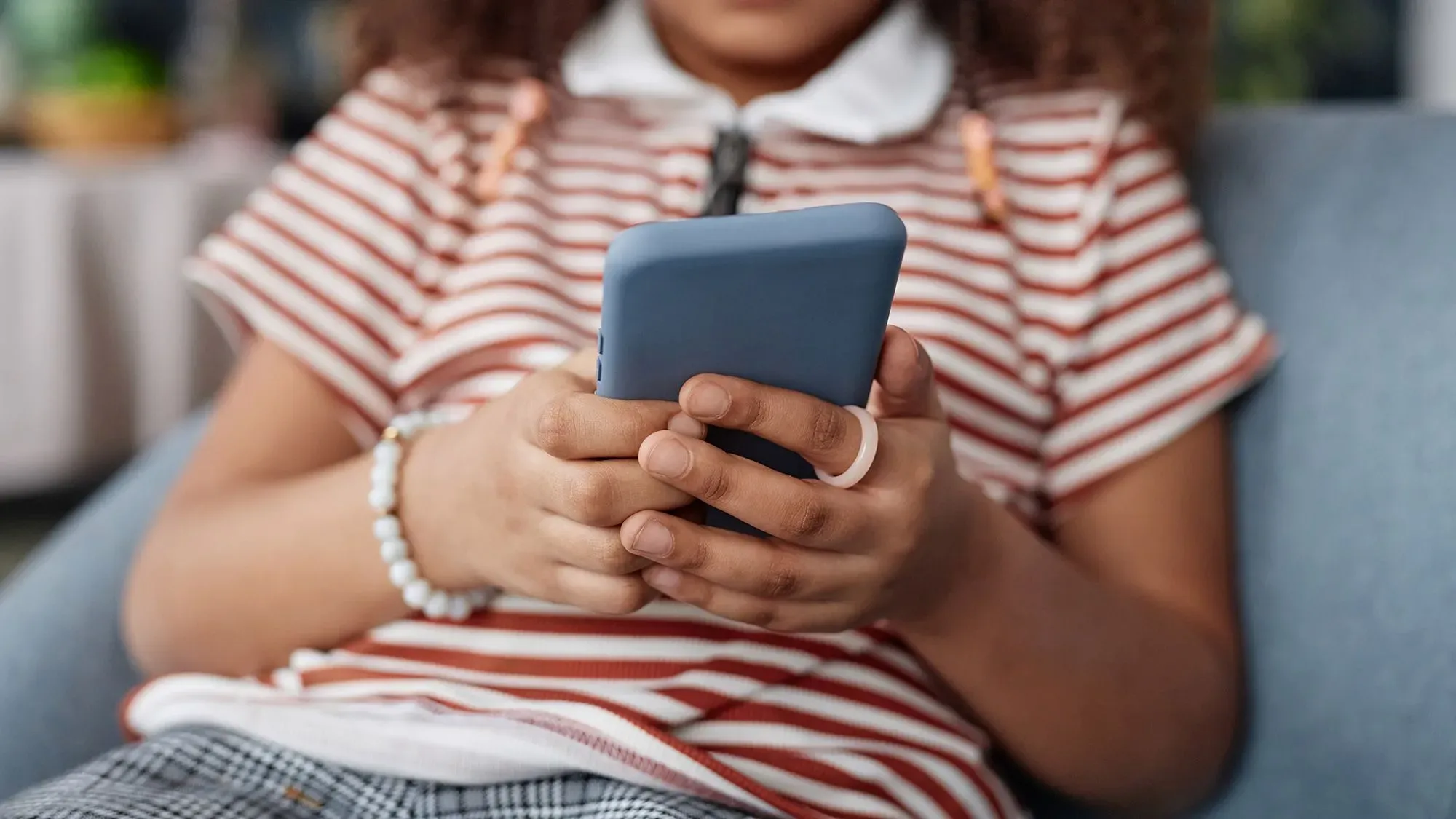 طفل صغير يجلس على أريكة، ممسكًا بهاتف ذكي، مما يعكس تأثير التكنولوجيا على الأطفال وزيادة مخاطر الاعتداء الجنسي عبر الإنترنت.