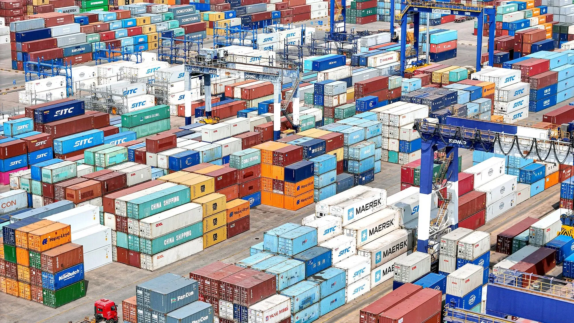 صورة لميناء حاويات مزدحم، حيث تتكدس حاويات الشحن المتنوعة، تعكس تأثير الرسوم الجمركية المتبادلة بين الصين والولايات المتحدة.