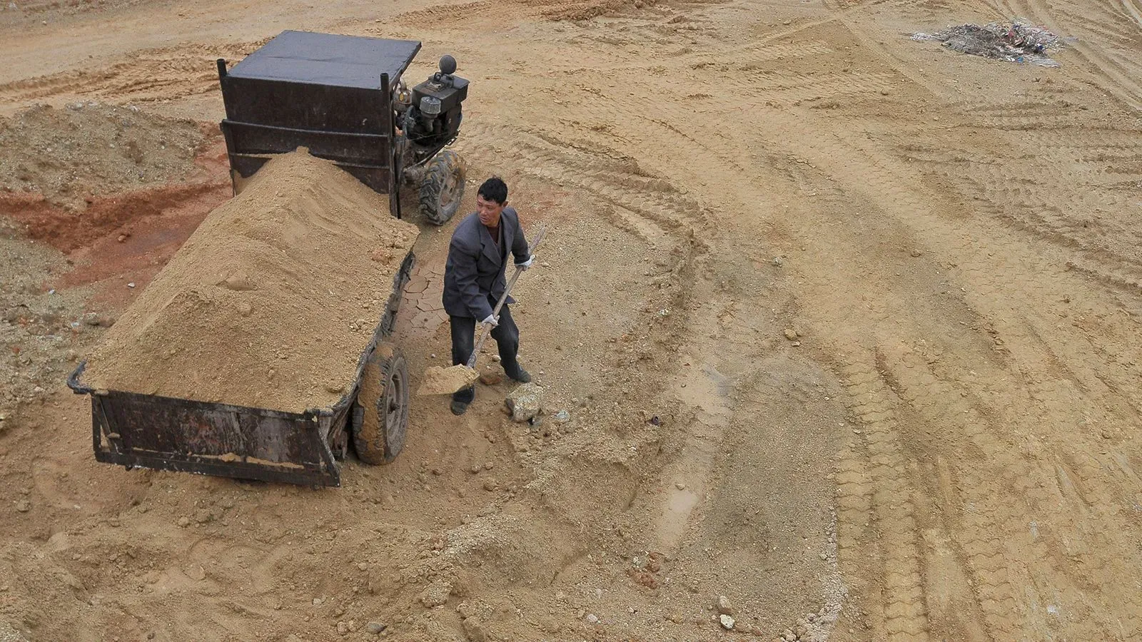 عامل يعمل على تحميل الرمل في عربة على أرضية غير مستوية، مما يعكس أنشطة استخراج المعادن في الصين وسط ضوابط التصدير.