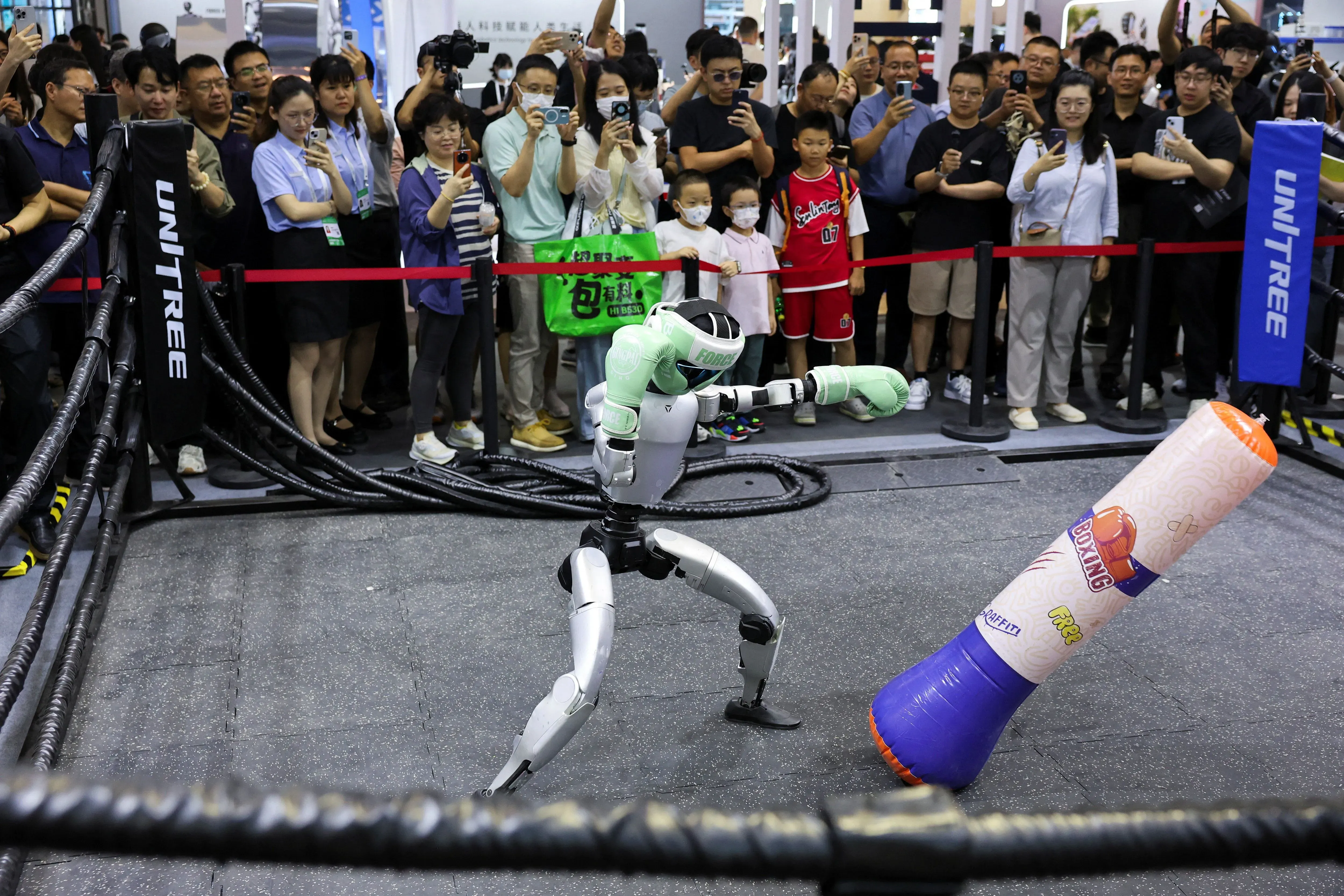 روبوت يتدرب على الملاكمة داخل حلبة، بينما يتجمع جمهور من الناس لمشاهدته، مما يعكس اهتمام الصين المتزايد في مجال الذكاء الاصطناعي.