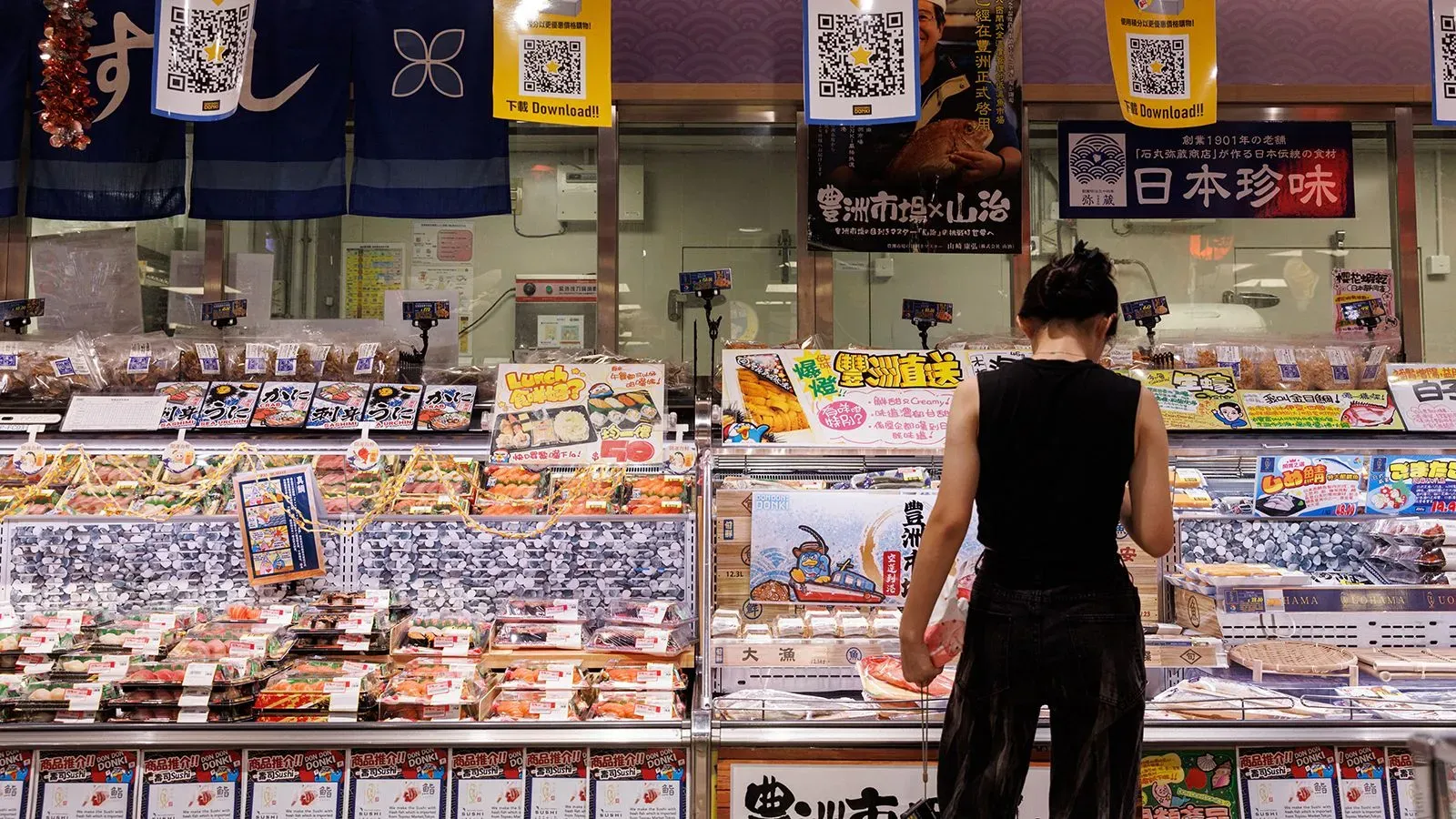 امرأة تتسوق في متجر للمأكولات البحرية، معروضات متنوعة من الأطعمة البحرية اليابانية، تعكس تأثيرات قرار الصين بشأن الاستيراد.