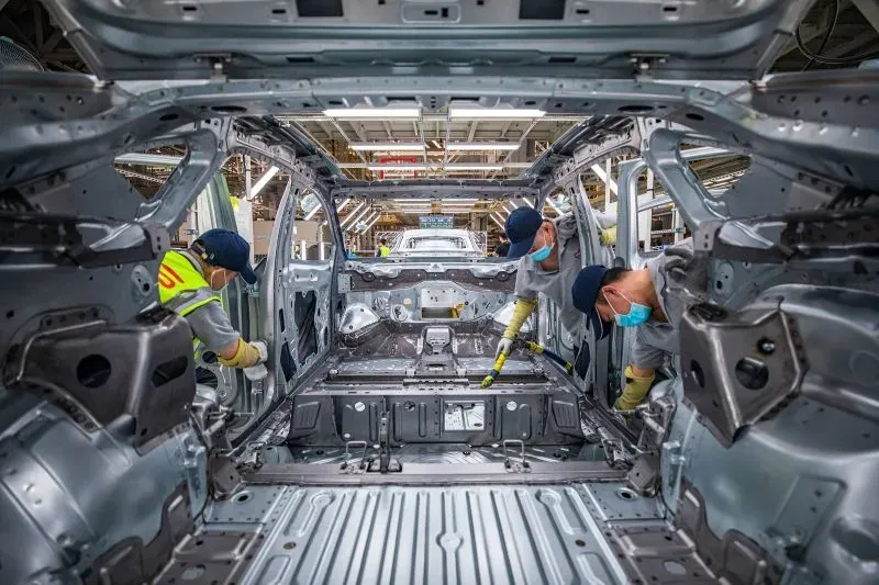 عمال في مصنع سيارات يقومون بتنظيف الهيكل المعدني لسيارة كهربائية جديدة، مما يعكس الابتكار في صناعة السيارات بالصين.