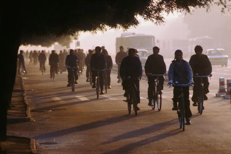 مجموعة من الأشخاص يركبون الدراجات في شارع مزدحم، مع وجود سيارات في الخلفية، مما يعكس تطور وسائل النقل في الصين.