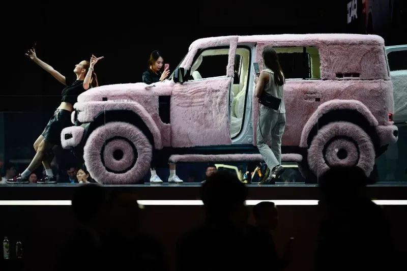 سيارة كهربائية مغطاة بالفرو الوردي تعرض في معرض شنغهاي للسيارات، مع زوار يتفاعلون حولها، مما يعكس الابتكار في صناعة السيارات الصينية.