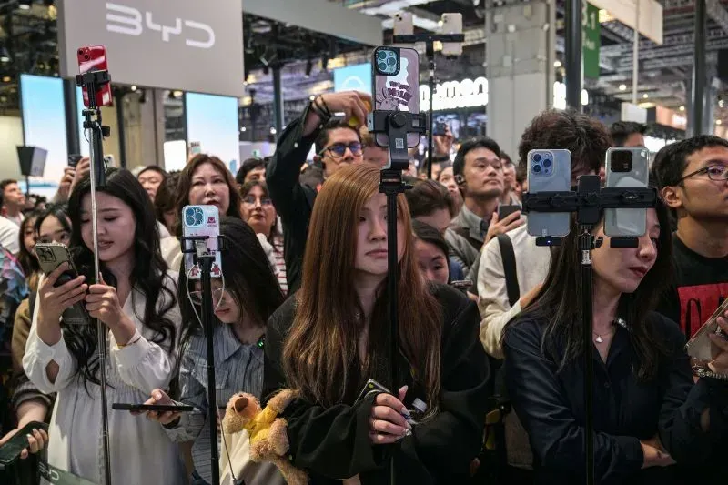 حشد كبير من الزوار في معرض شنغهاي للسيارات، يستخدمون الهواتف الذكية لتوثيق عرض السيارات الكهربائية الجديدة من شركة BYD.