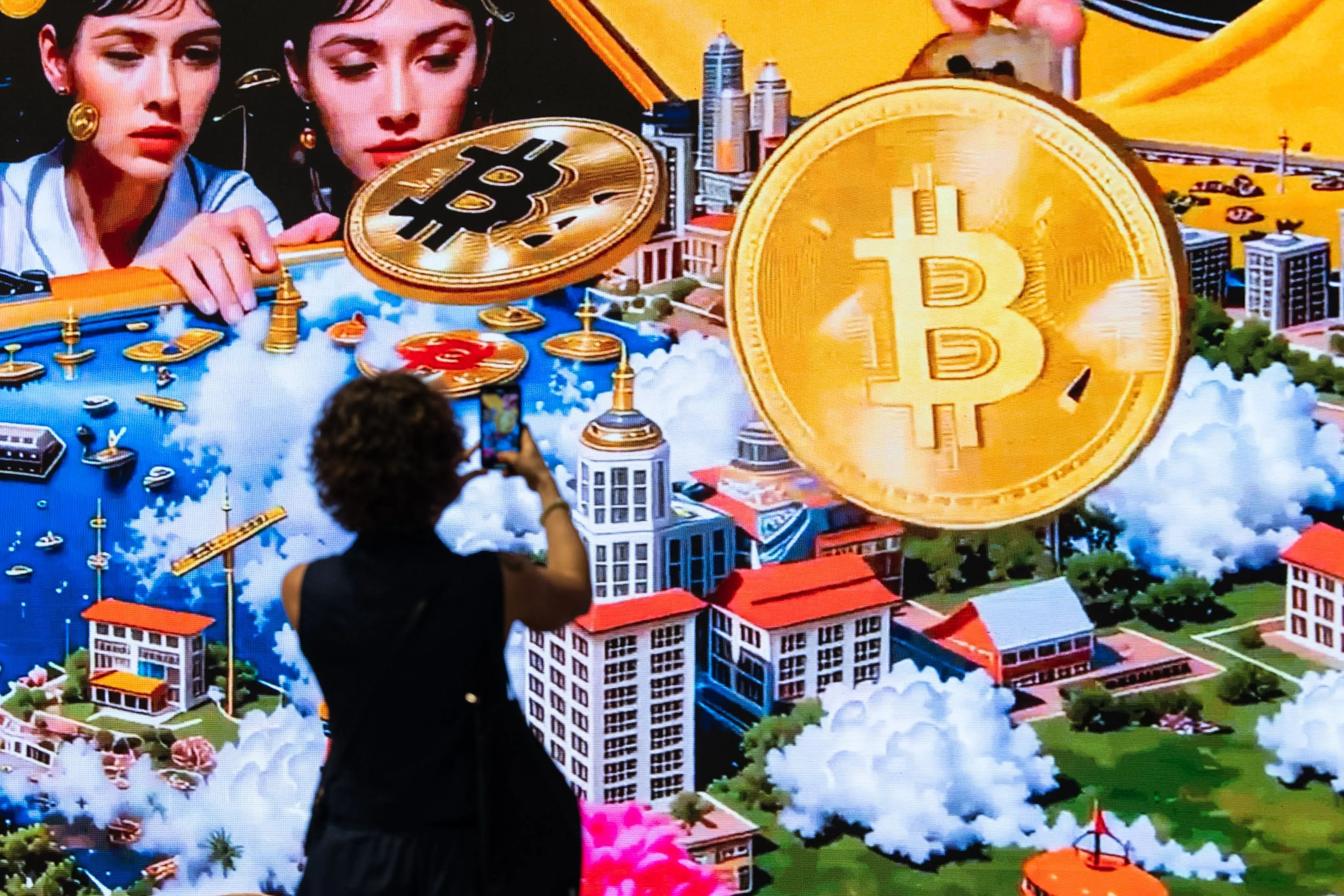 امرأة تلتقط صورة أمام شاشة ضخمة تعرض رموز بيتكوين وصورًا تعكس تطور العملات الرقمية في هونغ كونغ.