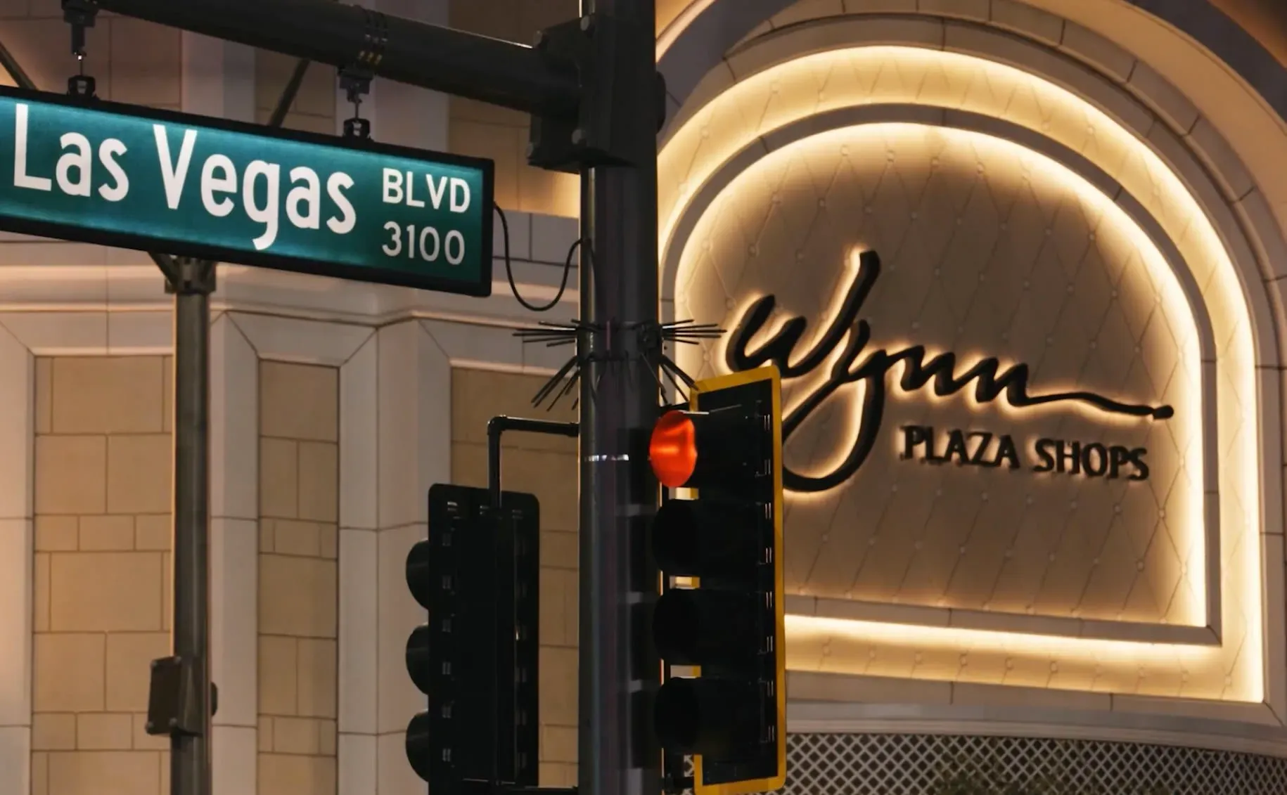 لافتة شارع لاس فيغاس مع إشارة حمراء، خلفها واجهة كازينو وين بلازا المتألقة، تعكس أجواء الحياة الليلية في المدينة.