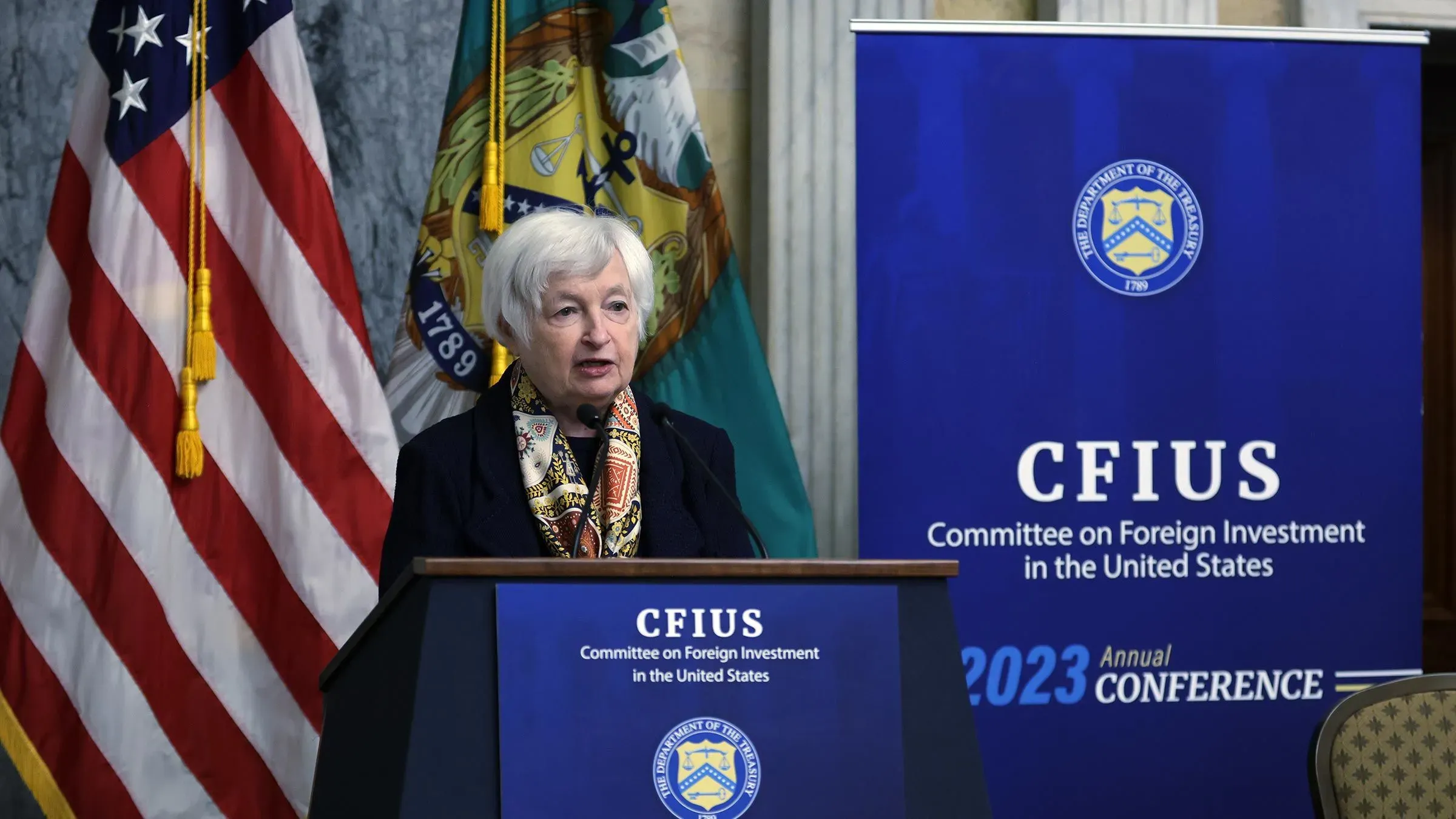 وزيرة الخزانة جانيت يلين تتحدث في مؤتمر لجنة الاستثمار الأجنبي في الولايات المتحدة (CFIUS) 2023، مع العلم الأمريكي خلفها.