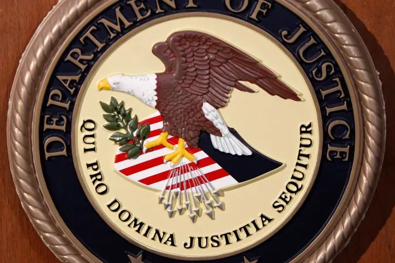 شعار وزارة العدل الأمريكية يظهر النسر الأمريكي مع درع يحمل ألوان العلم، يرمز إلى العدالة والأمن القانوني.