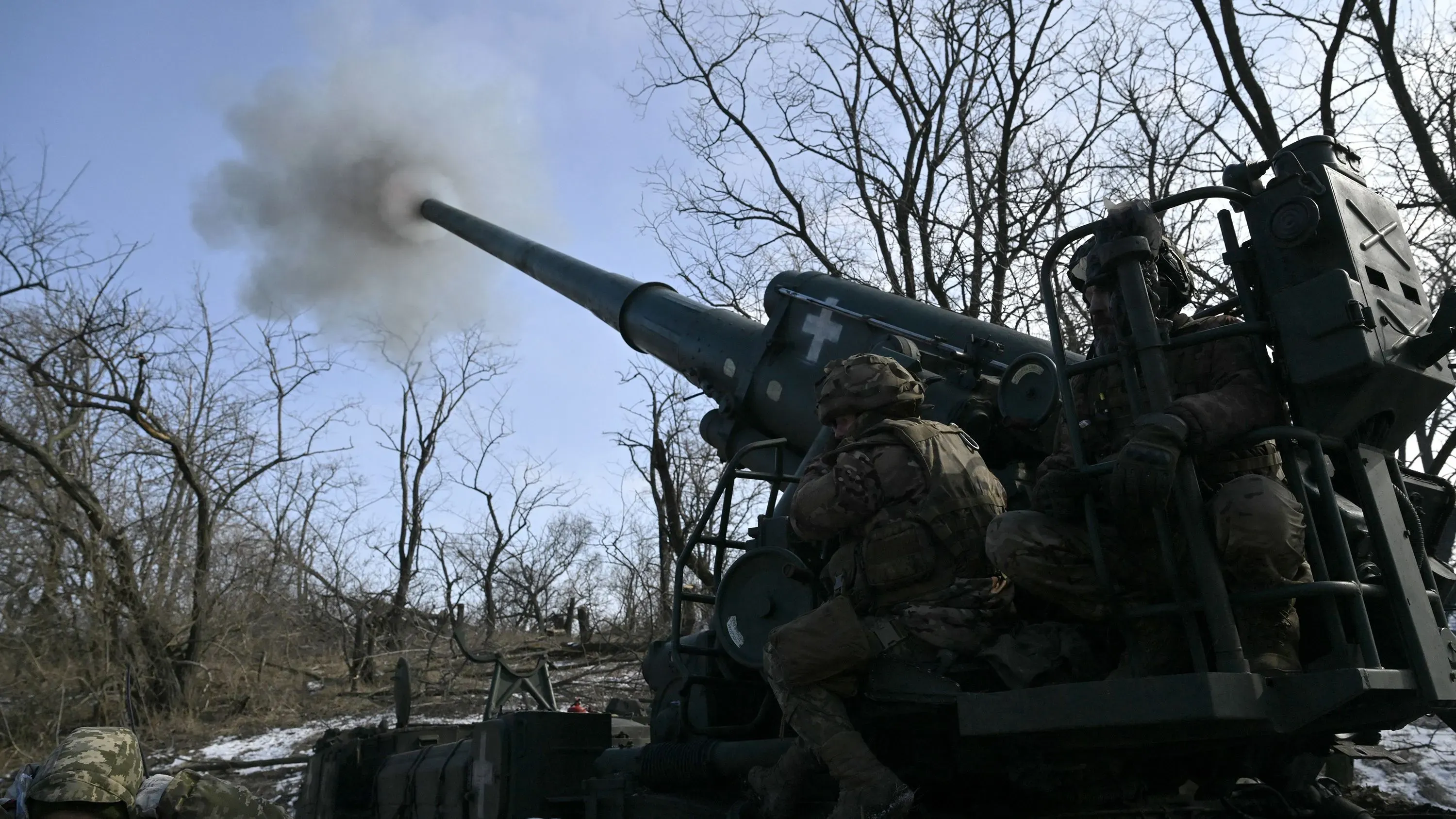 جنود أوكرانيون يقومون بتشغيل مدفع ميداني في منطقة مشجرة، مع تصاعد الدخان من فوهة المدفع، في سياق الصراع العسكري الحالي.