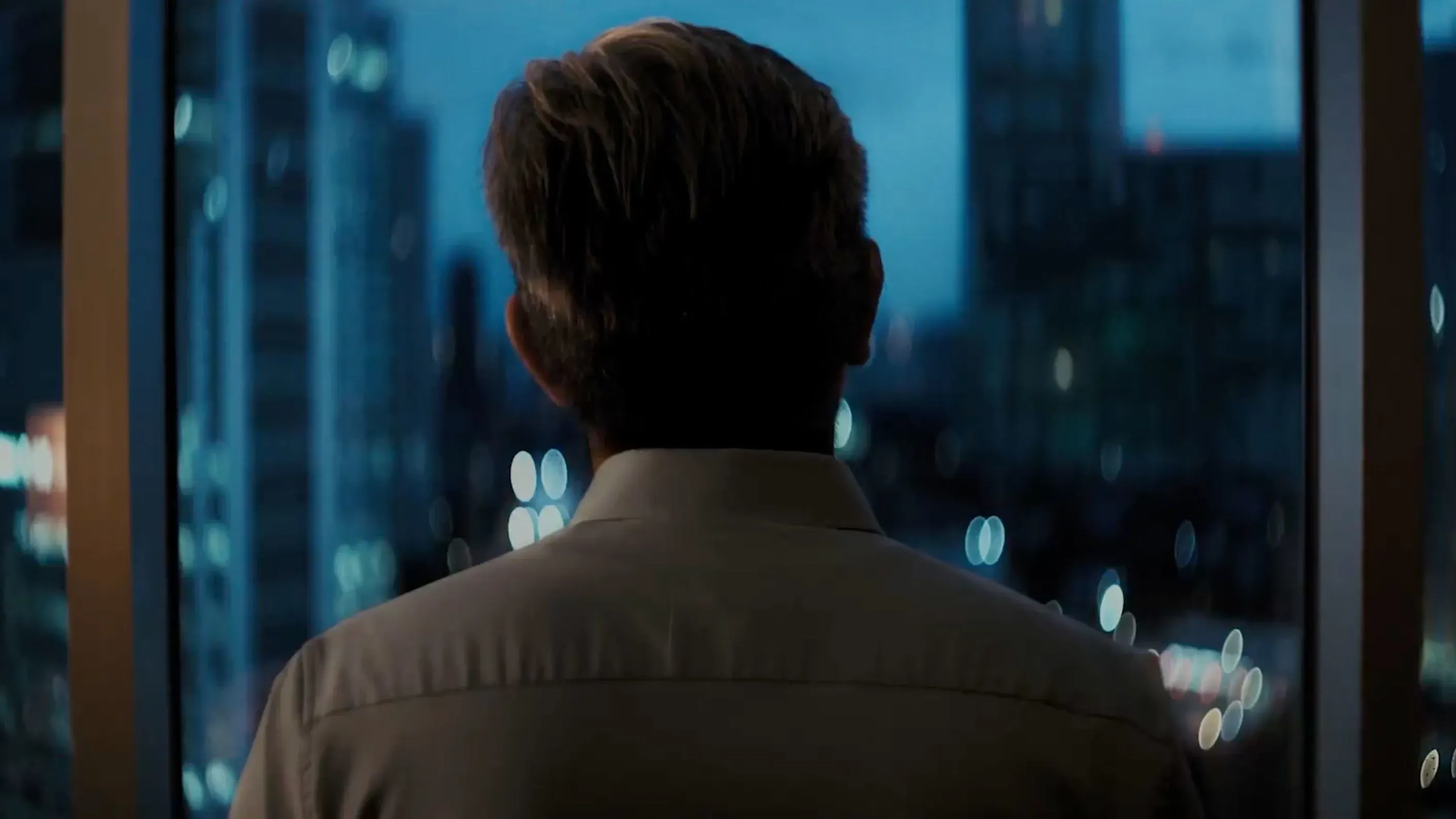 رجل ينظر من نافذة إلى مدينة مضاءة ليلاً، يعكس شعور القلق والتوتر في ظل التحديات السياسية والاقتصادية.