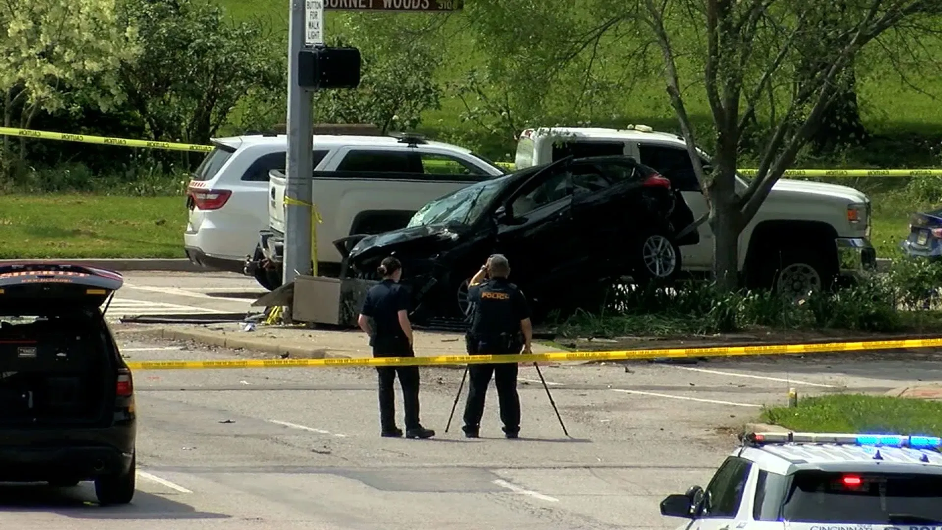 حادث سير يظهر سيارة سوداء متضررة ترتفع فوق الرصيف، مع وجود ضباط شرطة في موقع الحادث، حيث وقع الحادث بالقرب من جامعة سينسيناتي.