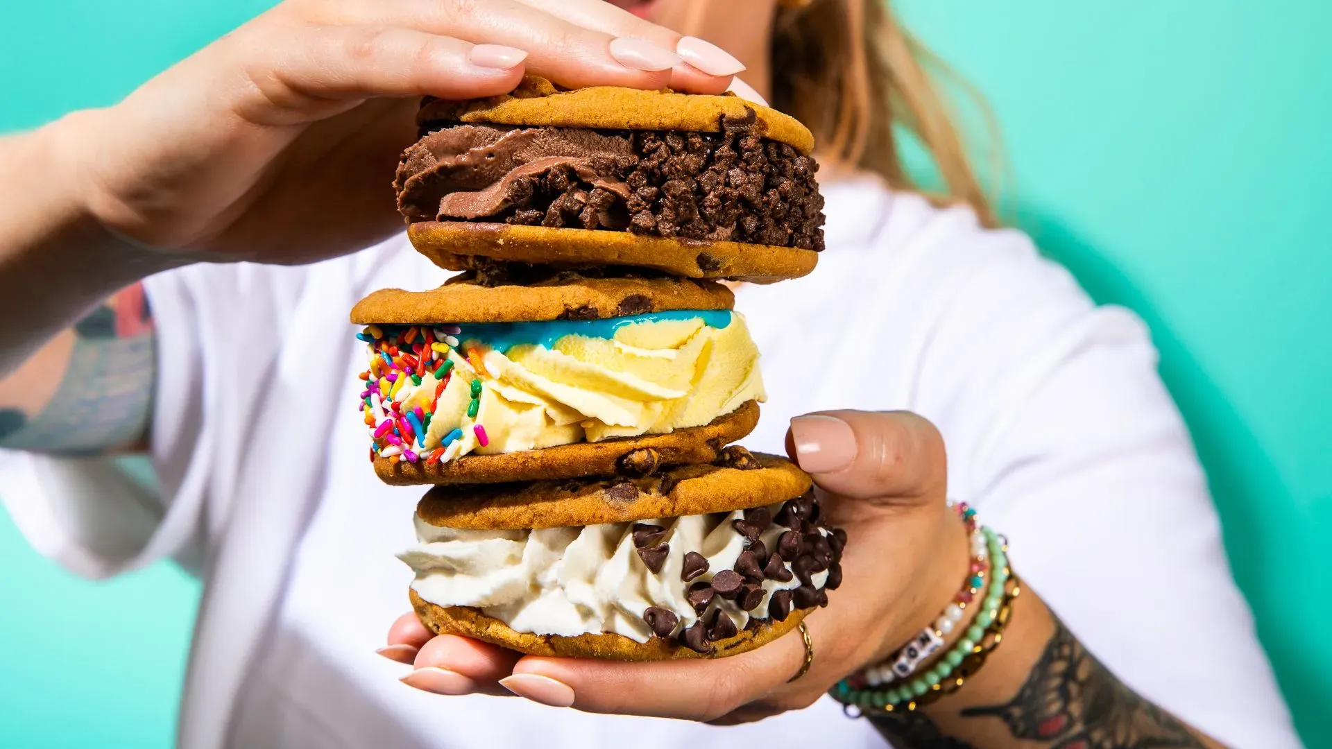 سيدة تحمل مجموعة من السندويشات المكونة من بسكويت محشو بآيس كريم ملون، مع خلفية زاهية تعكس ثقافة المتعة الصغيرة.