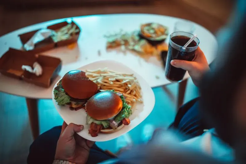 وجبة سريعة تتكون من برجرين مع بطاطا مقلية وكوب من المشروب الغازي، مع بقايا طعام على الطاولة، تعكس تأثير الأطعمة فائقة المعالجة.