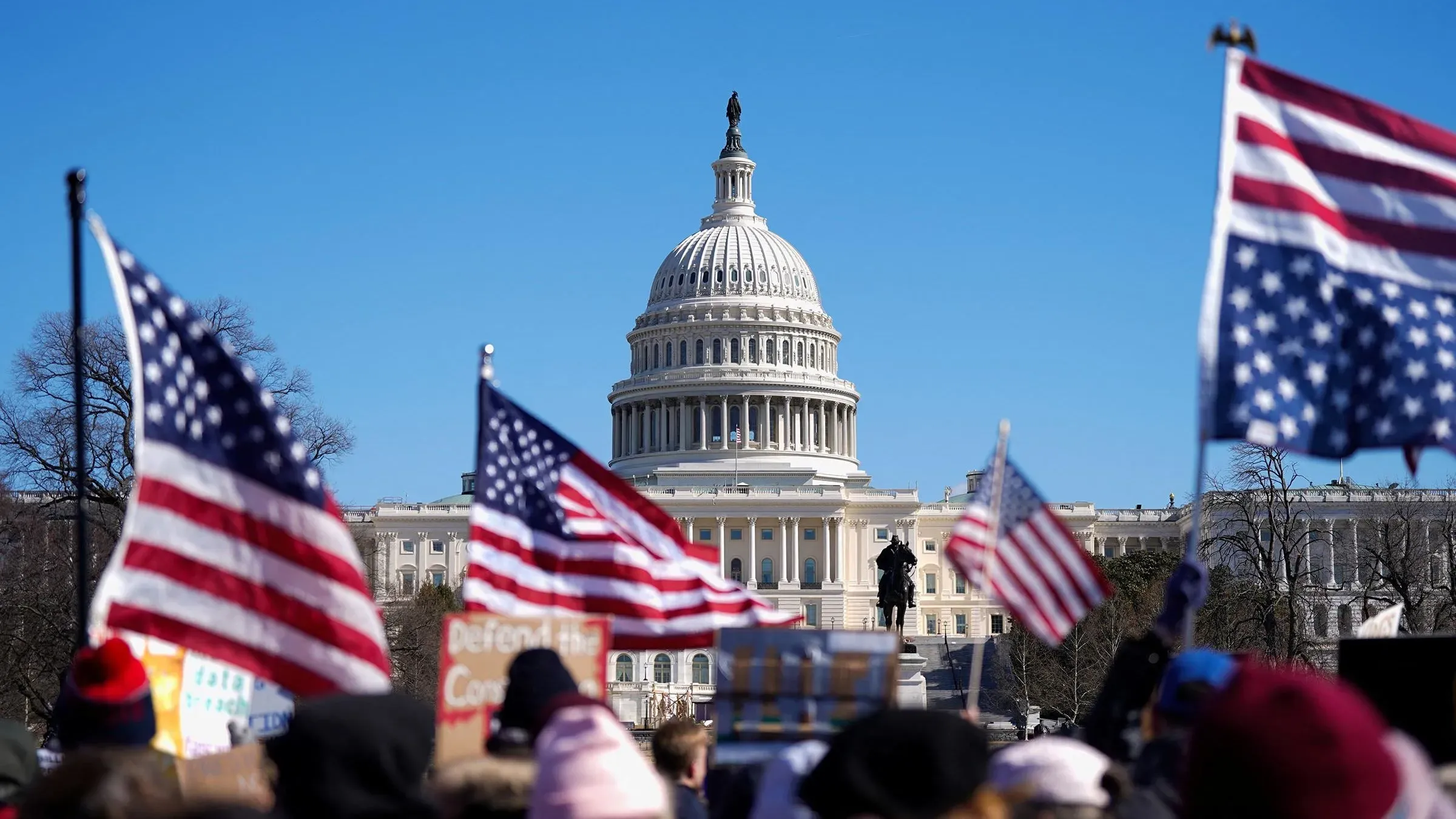 تظهر الصورة مبنى الكابيتول الأمريكي مع مجموعة من المتظاهرين يحملون الأعلام الأمريكية، مما يعكس الإحباط العام من السياسة الحالية.