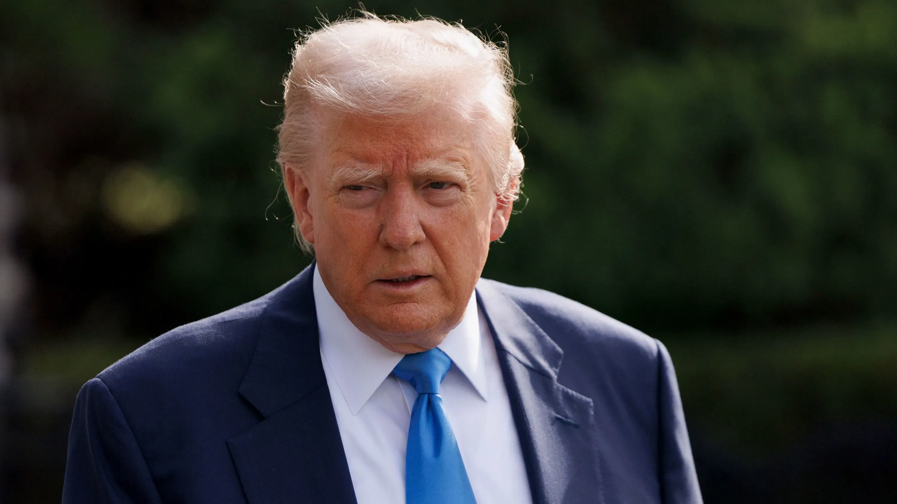 دونالد ترامب يظهر في صورة جادة، مرتديًا بدلة زرقاء وربطة عنق زرقاء، مع خلفية خضراء، مما يعكس تراجع شعبيته في استطلاعات الرأي حول إدارته.