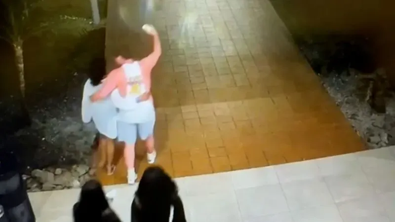 صورة تظهر مجموعة من الشباب يسيرون معًا في منتجع ليلي، حيث يبدو شخصان يتبادلان القبل في الخلفية.