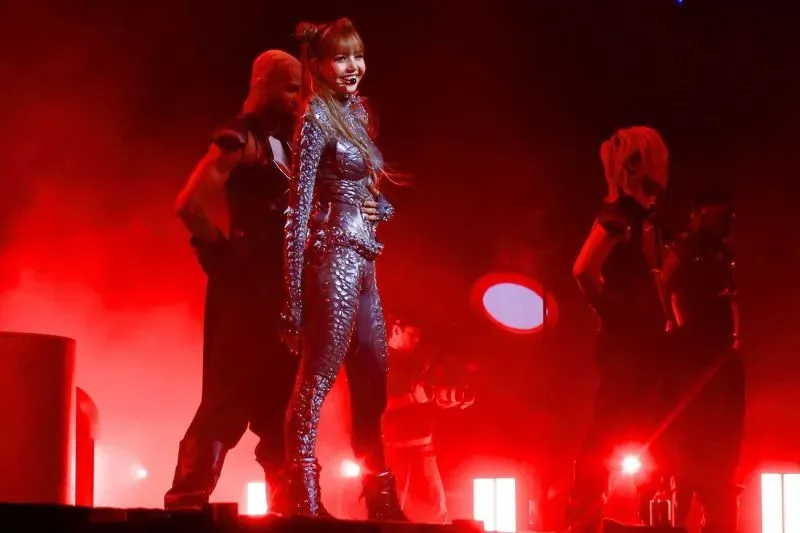 ليزا من فرقة بلاك بينك تؤدي على المسرح في كوتشيلا، مرتدية بدلة لامعة مستوحاة من الحيوانات، وسط أضواء حمراء ساطعة.