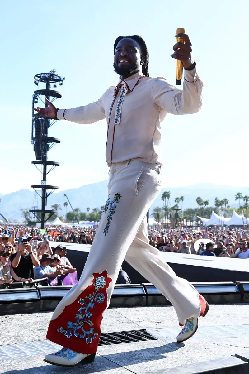 مغني يرتدي بدلة مزينة بألوان زاهية ويقدم عرضاً على المسرح في مهرجان كوتشيلا، محاطاً بجمهور كبير في أجواء احتفالية.