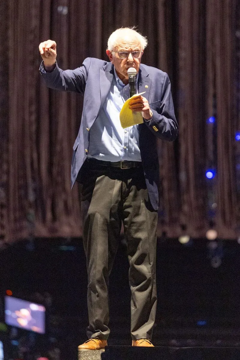 بيرني ساندرز يتحدث على المسرح في مهرجان كوتشيلا، مرتديًا سترة كحلية وقميص أزرق، مع ميكروفون في يده.