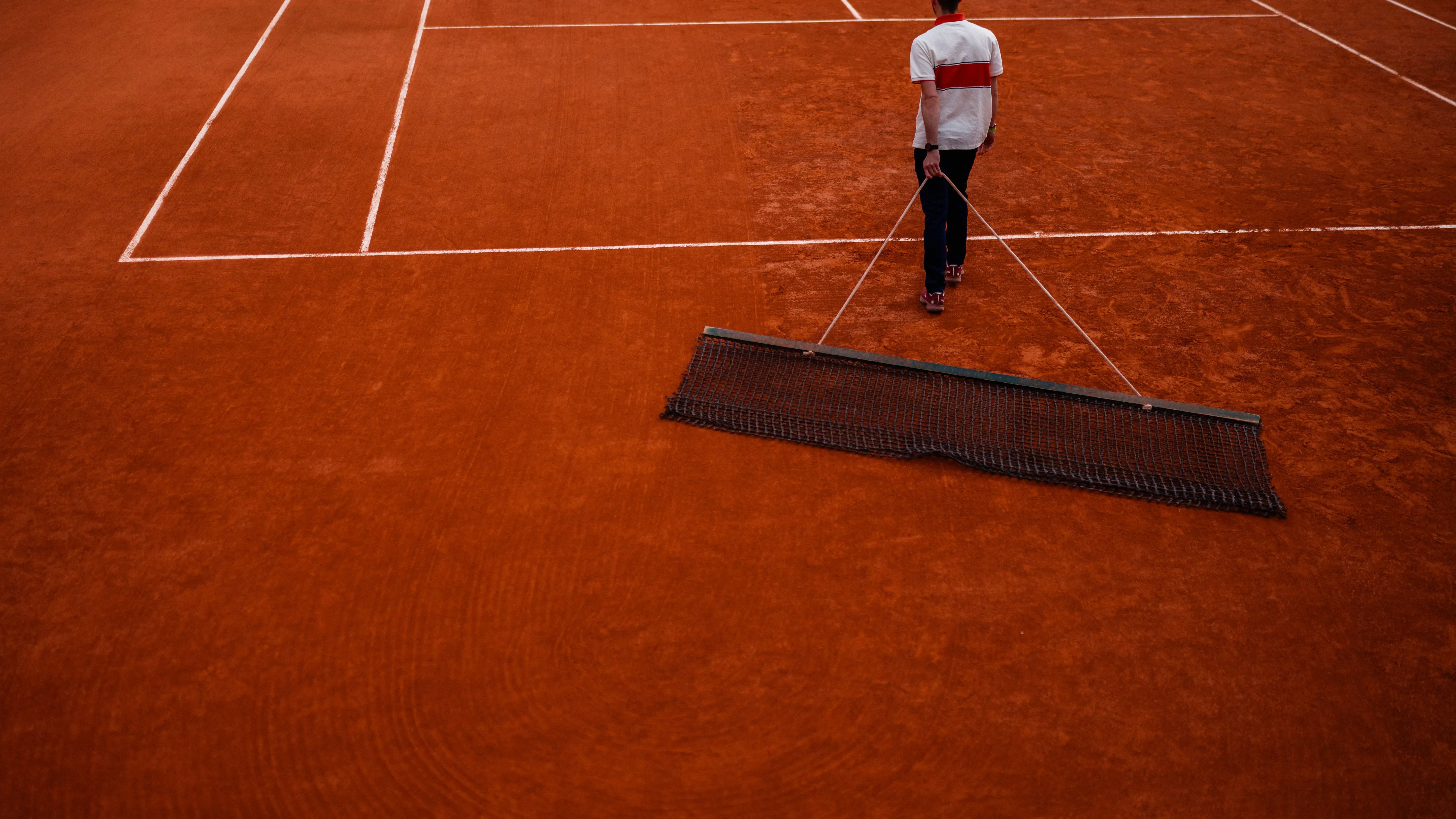 شخص يحمل أداة لتنظيف أرضية ملعب التنس الطيني، حيث يستعد الملعب لاستقبال اللاعبين في بطولة فرنسا المفتوحة.