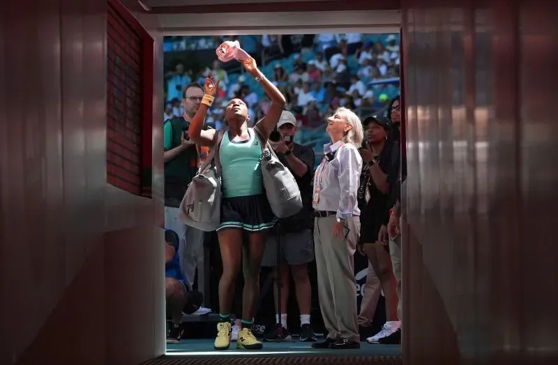 تظهر كوكو جوف وهي تستعد للمباراة في بطولة ميامي المفتوحة، حيث ترفع يدها نحو السماء بينما تراقبها الجماهير.