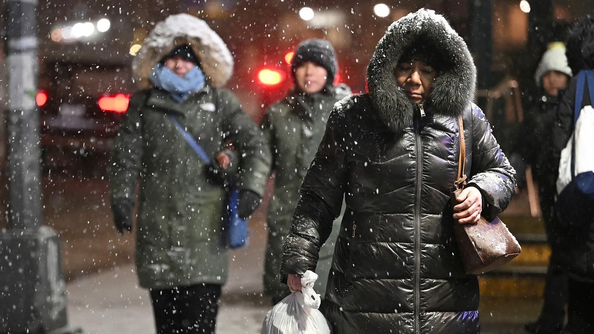 نساء يرتدين معاطف ثقيلة والثلوج تتساقط حولهن، في سياق عاصفة شتوية تجتاح الولايات المتحدة مع تحذيرات من الطقس البارد.