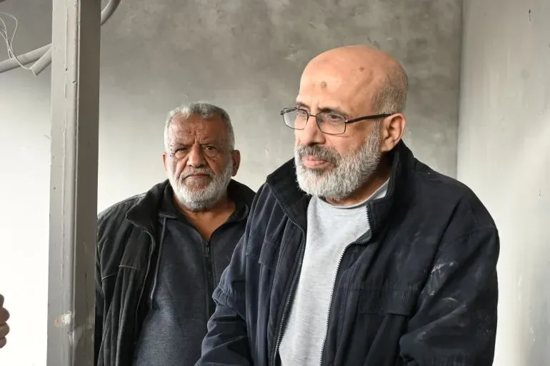 عائلة صنوبر في نابلس، تظهر مشاعر الحزن والقلق بعد هدم منزلهم، مع خلفية من الدمار الذي خلفه الانفجار.