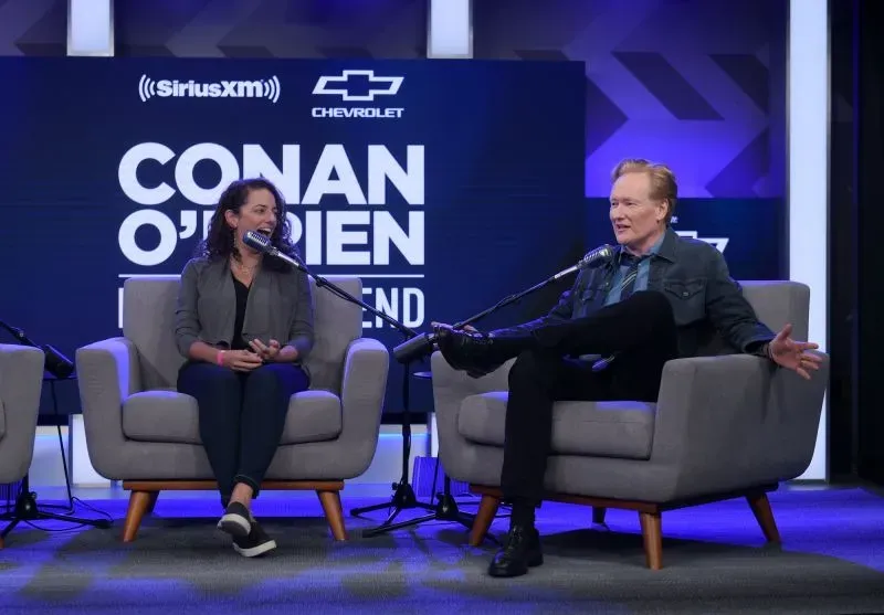 كونان أوبراين وسونا موفسيسيان يتحدثان خلال حلقة من البودكاست، مع خلفية تحمل شعار البرنامج، في أجواء تعكس تأثير حرائق الغابات في لوس أنجلوس.