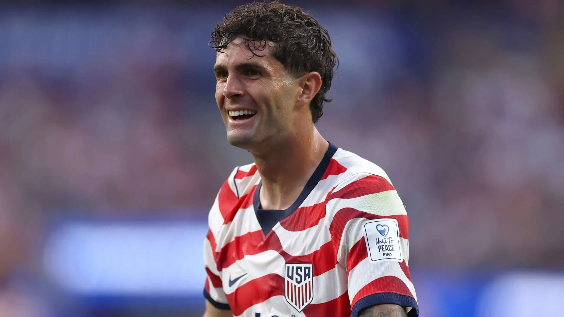 لاعب كرة قدم أمريكي يرتدي قميص منتخب الولايات المتحدة الأحمر والأبيض مبتسمًا خلال مباراة في كأس العالم 2022 بمنطقة CONCACAF.