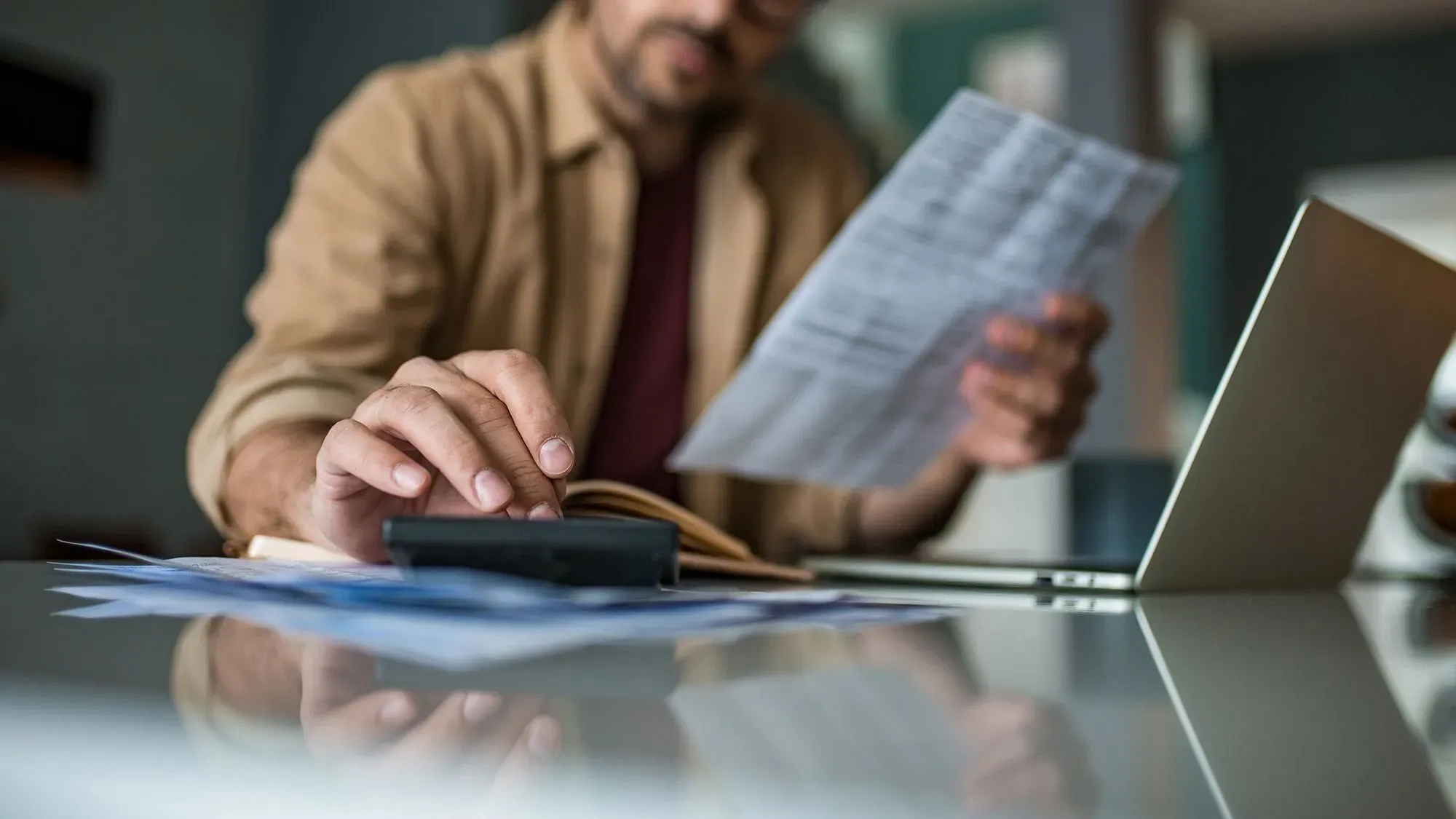 شخص يستخدم آلة حاسبة مع مستندات ضريبية وأوراق مالية، مما يعكس التحديات المرتبطة بالتغييرات الضريبية الحالية.