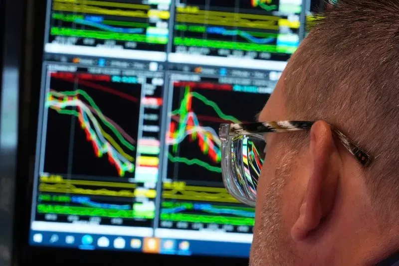 شخص يرتدي نظارات يراقب شاشات تعرض بيانات سوق الأسهم، مع تراجع ملحوظ في الرسوم البيانية. تعكس الصورة التقلبات الاقتصادية الحالية.