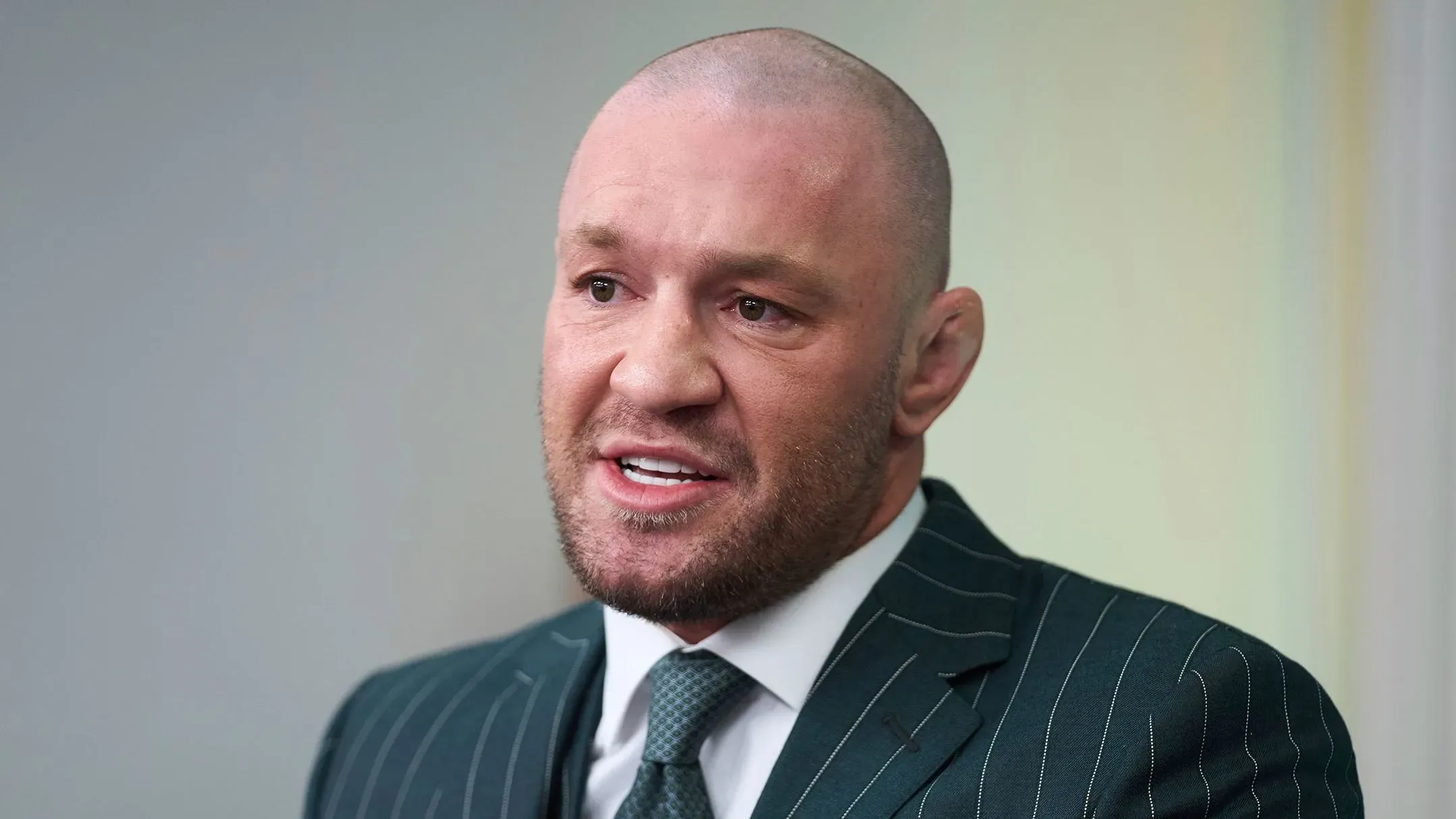 كونور ماكغريغور يتحدث بجدية، مرتديًا بدلة، في مناسبة تتعلق بترشحه للرئاسة الأيرلندية، مع التركيز على قضايا الهجرة.