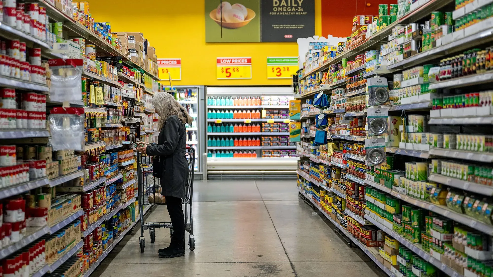 امرأة مسنّة تتسوق في ممر سوبرماركت مليء بالمنتجات الغذائية، تعكس تدهور ثقة المستهلكين في الاقتصاد الأمريكي.