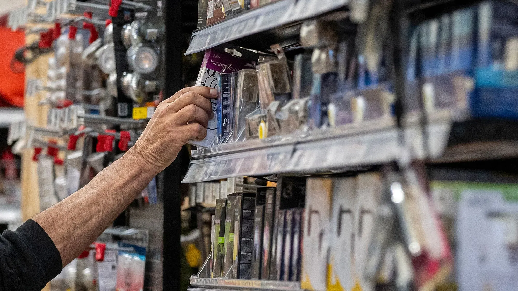 يد تظهر يد شخص تلتقط منتجًا من رف مليء بالسلع في متجر، مما يعكس تأثير عدم اليقين الاقتصادي على المستهلكين.