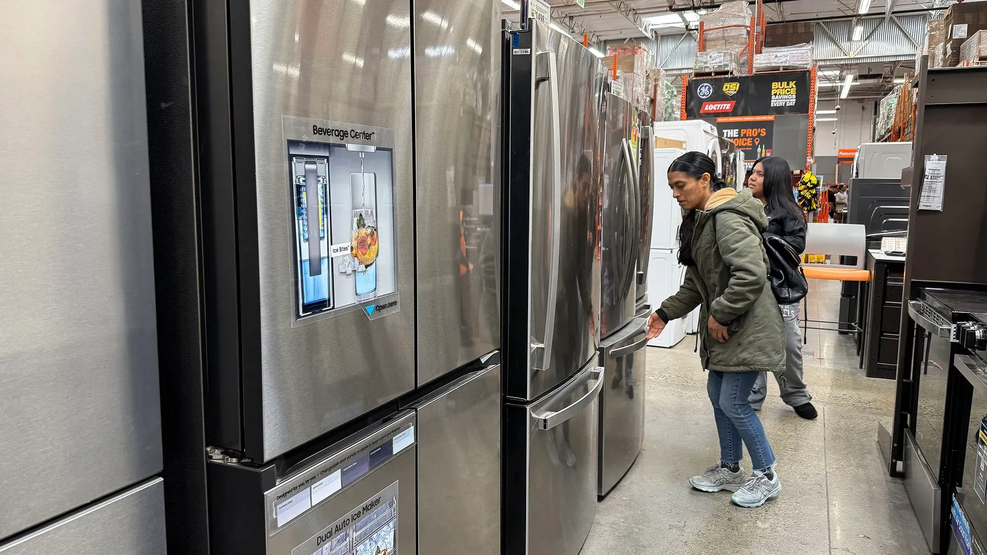 امرأة تتفقد ثلاجة في متجر للأجهزة المنزلية، مع وجود ثلاجات أخرى في الخلفية، تعكس زيادة إنفاق المستهلكين.