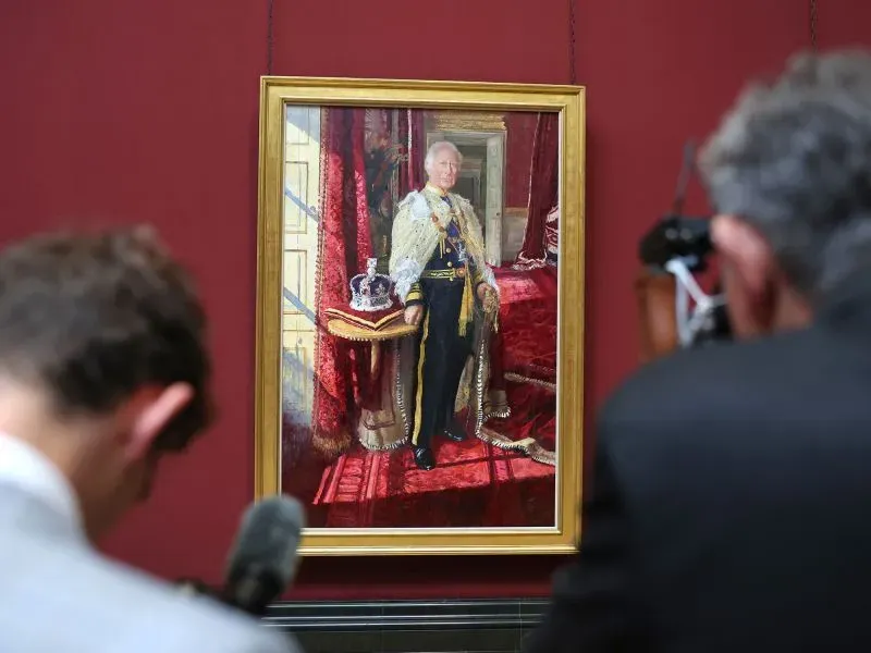 صورة رسمية لملك بريطانيا تشارلز، مرتديًا رداء الدولة، يقف بجانب التاج الإمبراطوري في قاعة العرش بقصر سانت جيمس.