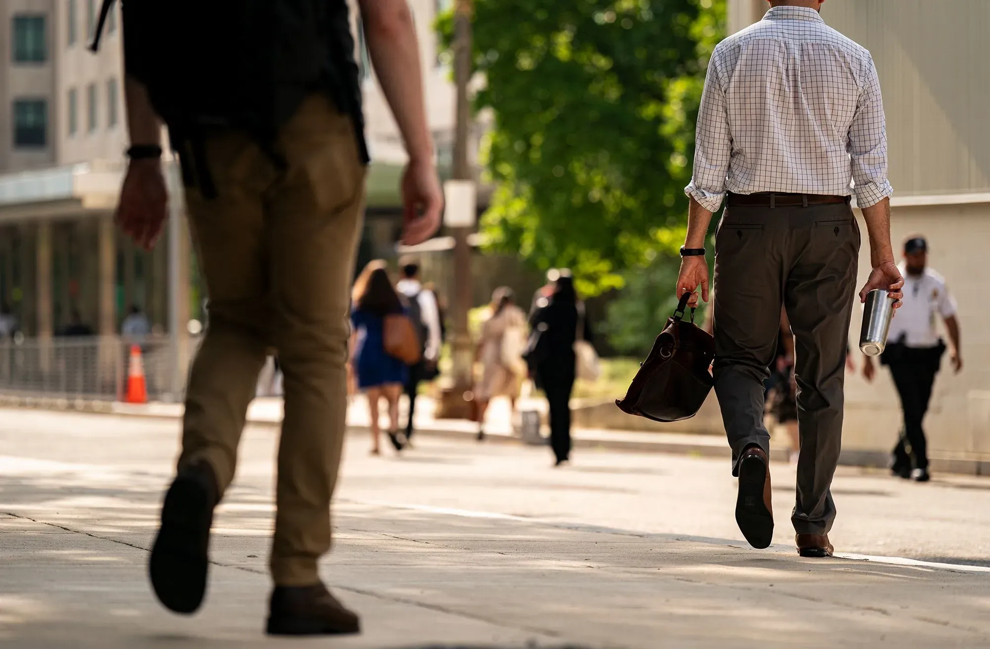 مشهد لعمال يسيرون في الشارع، مع التركيز على رجل يحمل حقيبة ومشروب، في سياق نقاش حول حقوق العمال والنقابات.