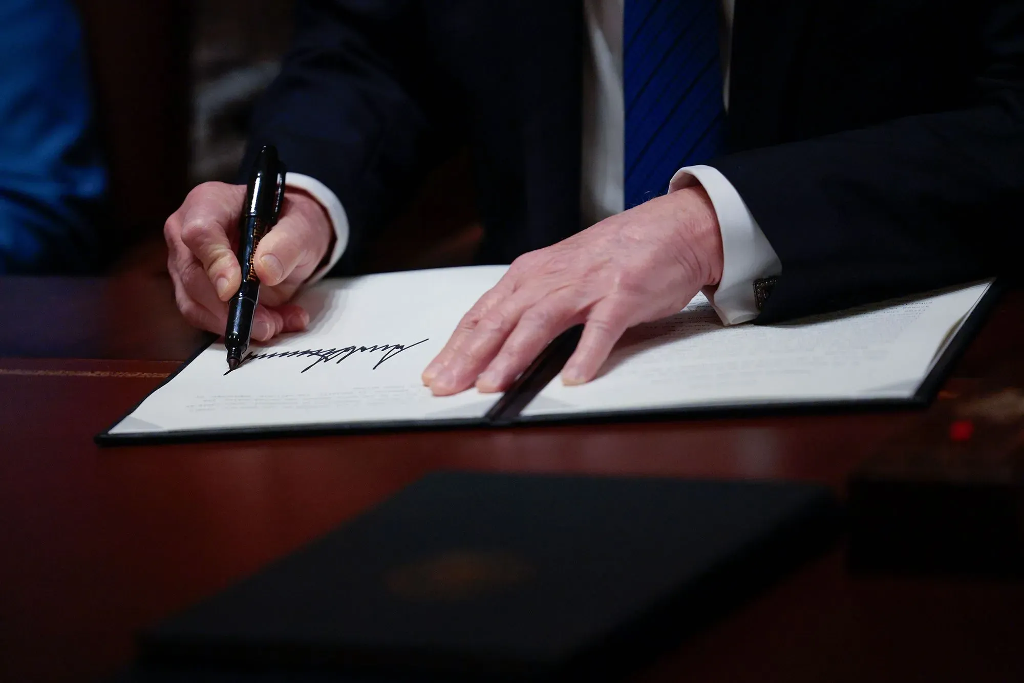 تظهر الصورة يد شخص ترتدي بدلة رسمية، وهو يوقع على وثيقة رسمية، مما يعكس تأثير السياسات على حقوق العمال النقابيين.