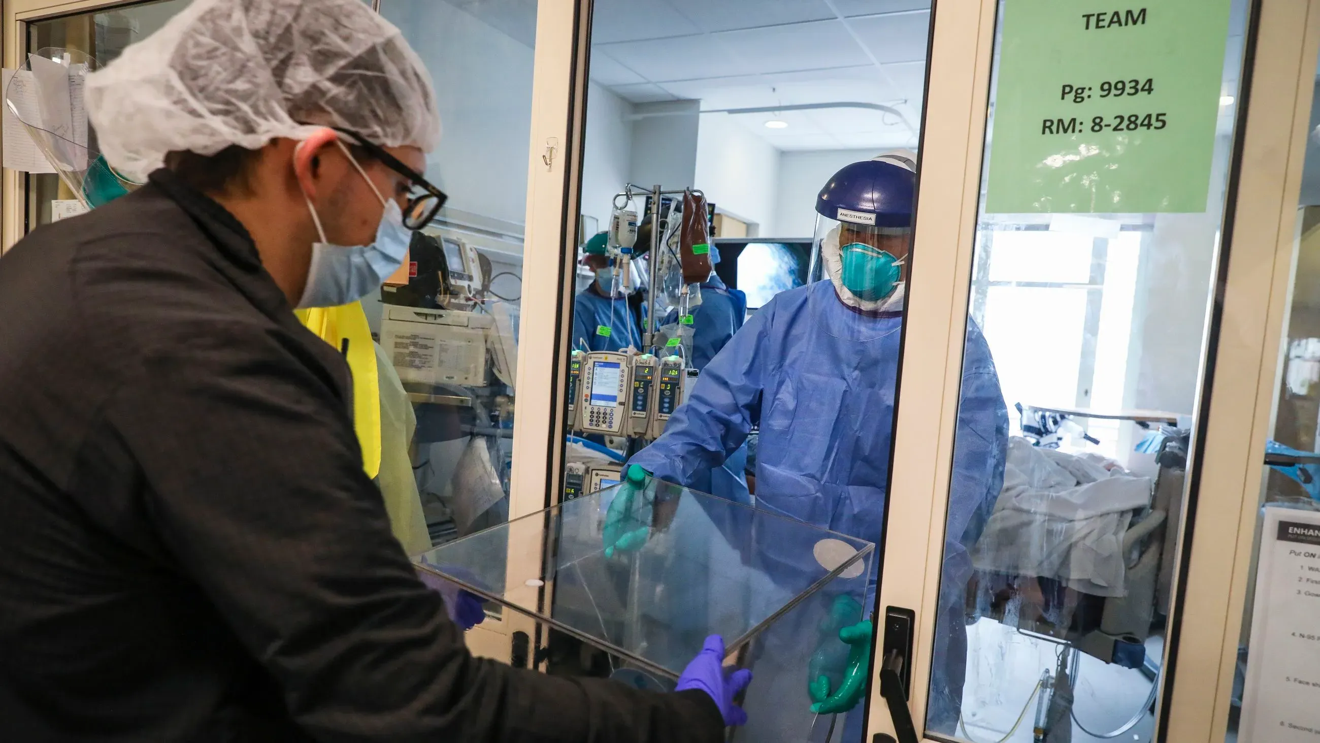 عامل صحي يرتدي معدات واقية ينقل جهاز طبي إلى غرفة مريض في مستشفى، في إطار جهود مواجهة الأوبئة وتعزيز التعاون الصحي العالمي.