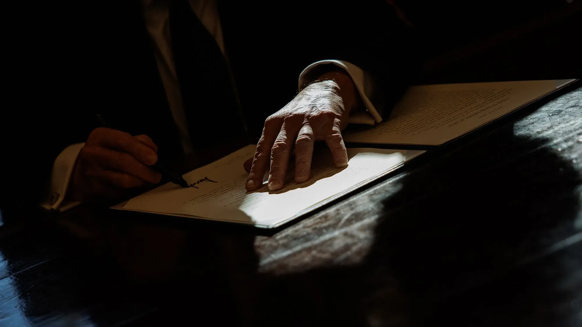 يد تظهر يد شخص تكتب على ورقة، مع تسليط الضوء على الأثر السياسي والاقتصادي للقرارات الحكومية.