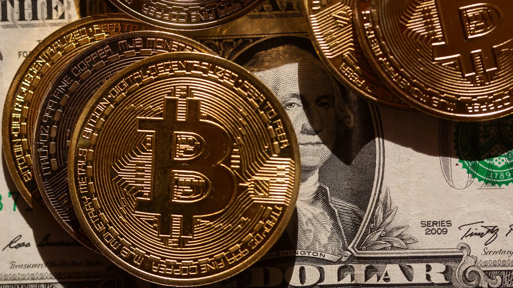 عملات بيتكوين ذهبية تتواجد فوق ورقة نقدية من الدولار الأمريكي، مما يرمز إلى تزايد اهتمام الحكومة الأمريكية بالعملات الرقمية.